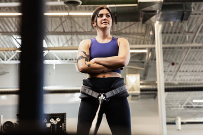 Woman in a gym wearing a sports bra and leggings with a weightlifting belt squat belt on.
