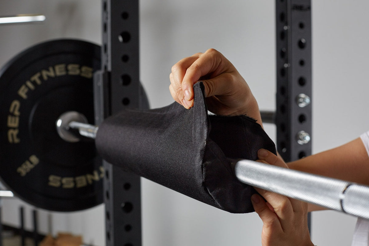 Lifter securing the REP barbell shoulder pad by velcroing it into place on a racked barbell.