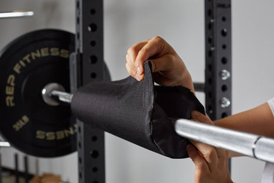 Lifter securing the REP barbell shoulder pad by velcroing it into place on a racked barbell.